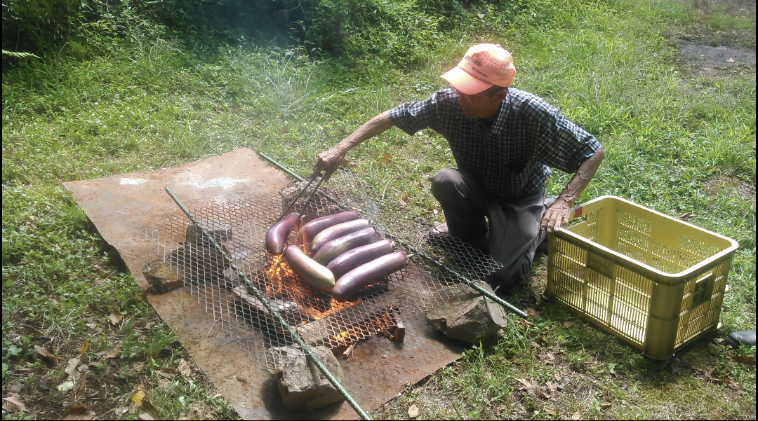 巨大な鈴ヶ沢なすを焼く生産者